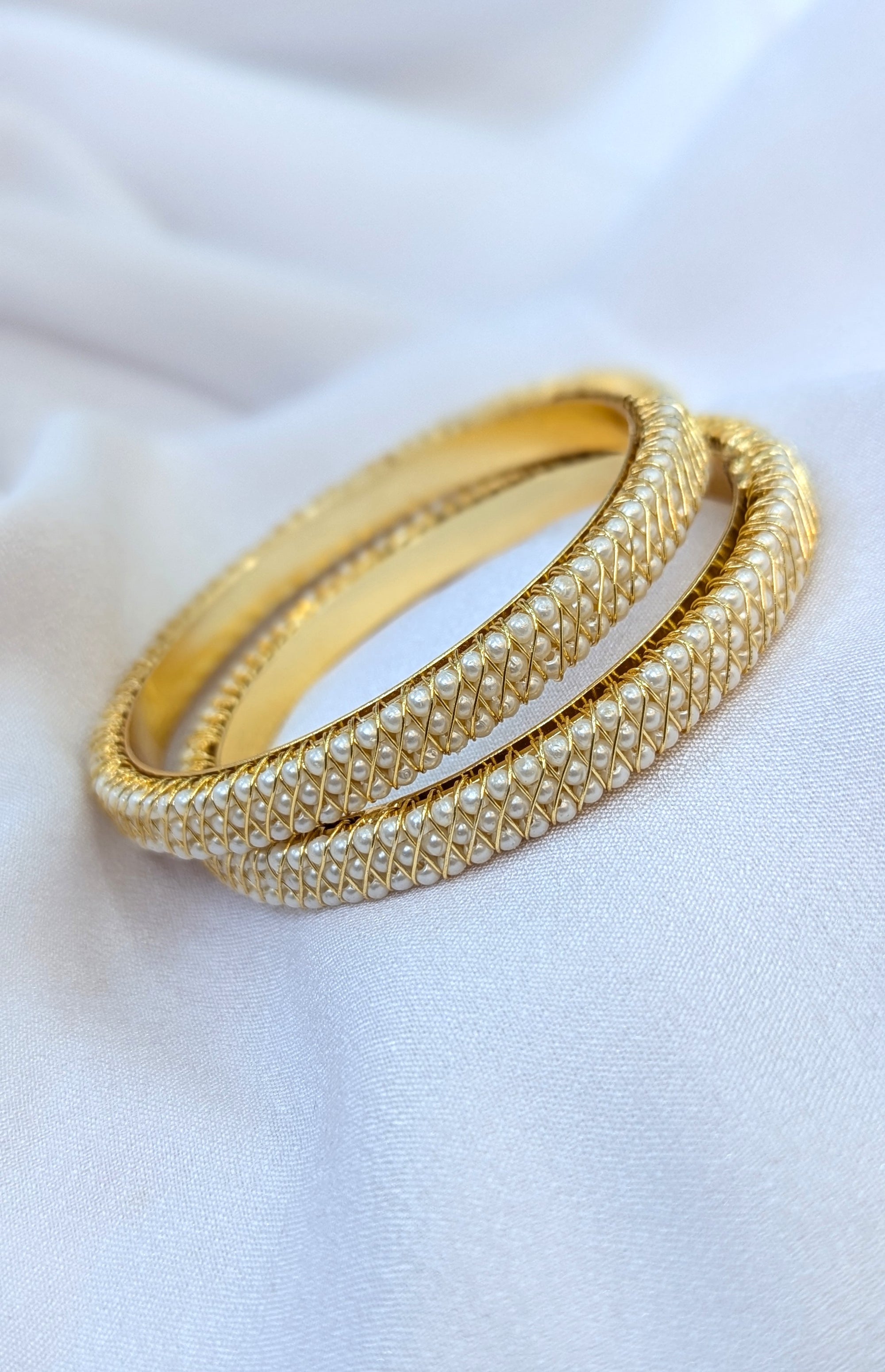 Two gold bangles on a white fabric background