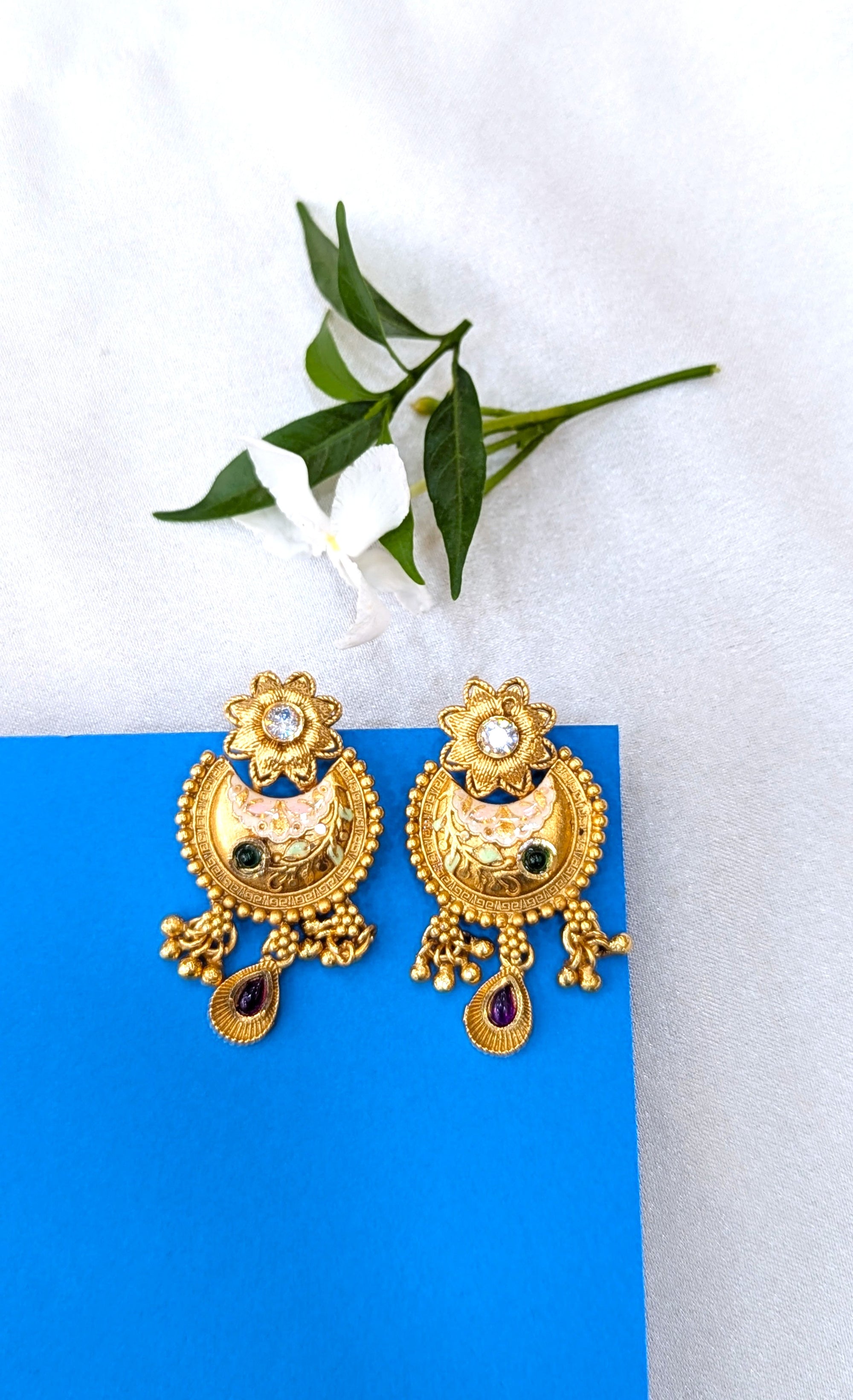 Gold earrings with black stones on a blue card with green leaves in the background