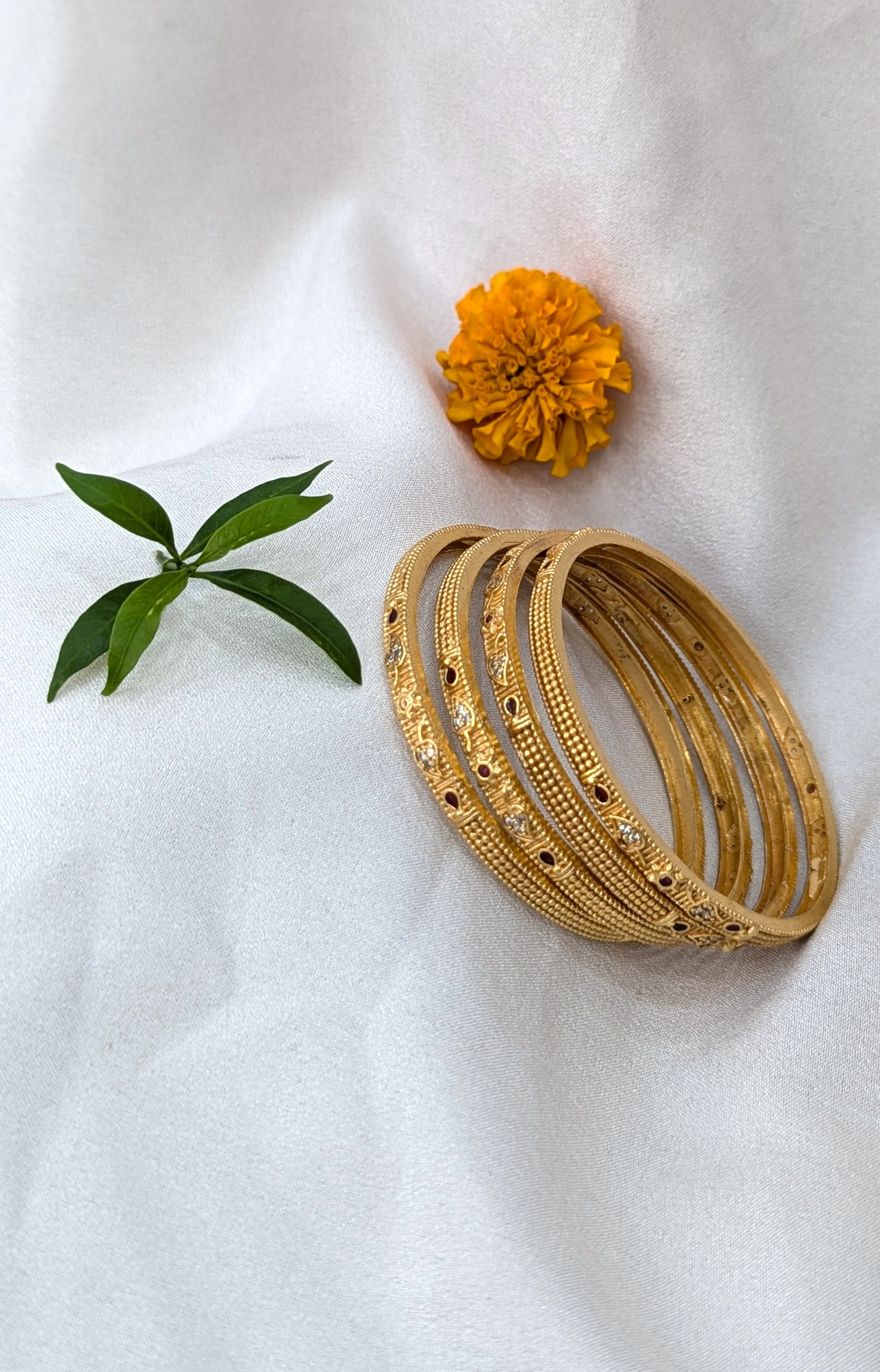 Set of gold bangles with a marigold flower and green leaf on a white background