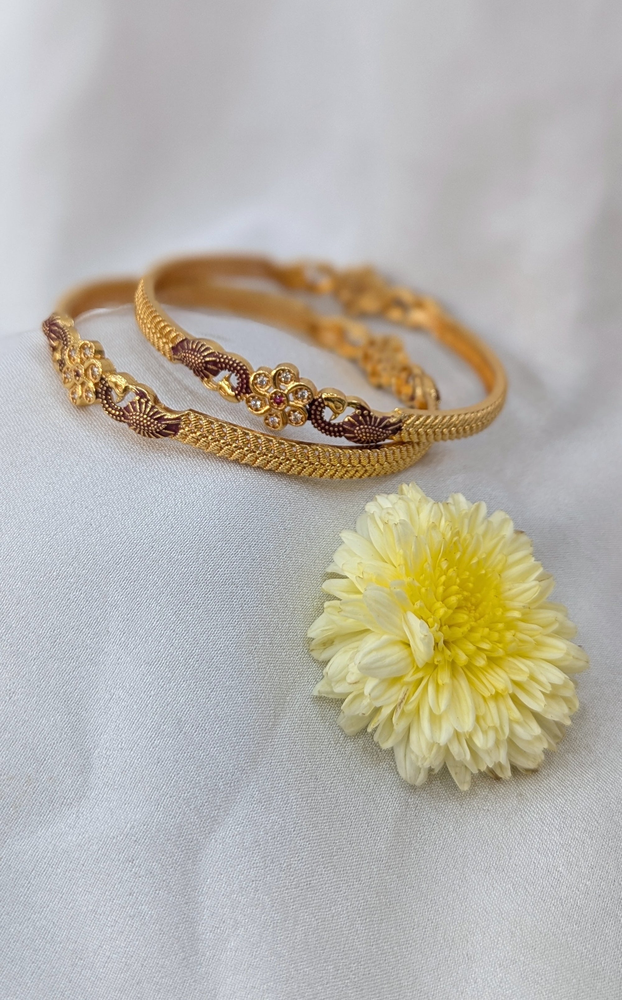 Gold bangles with a yellow flower on a light gray background