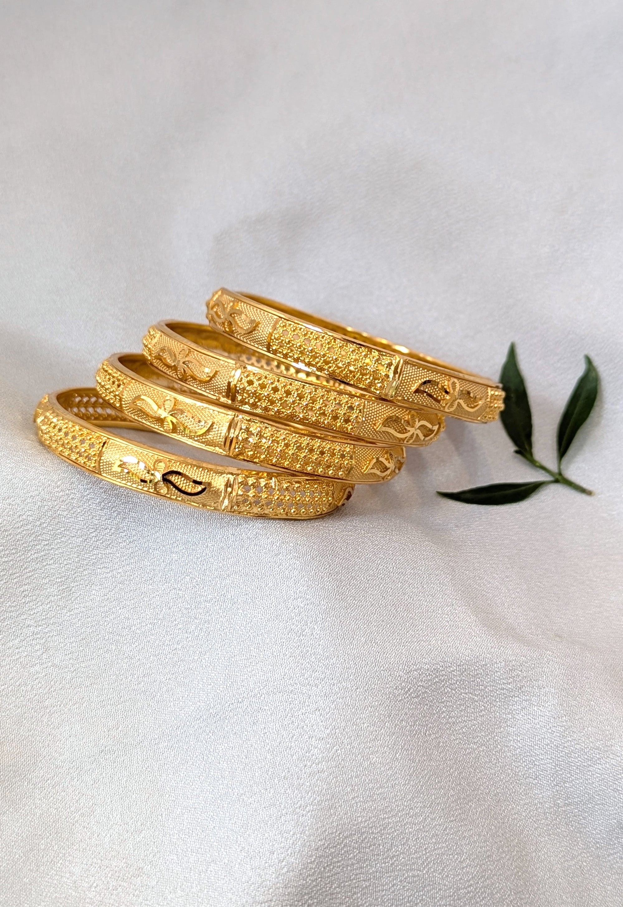 Set of gold bangles on a white fabric background with a green leaf.