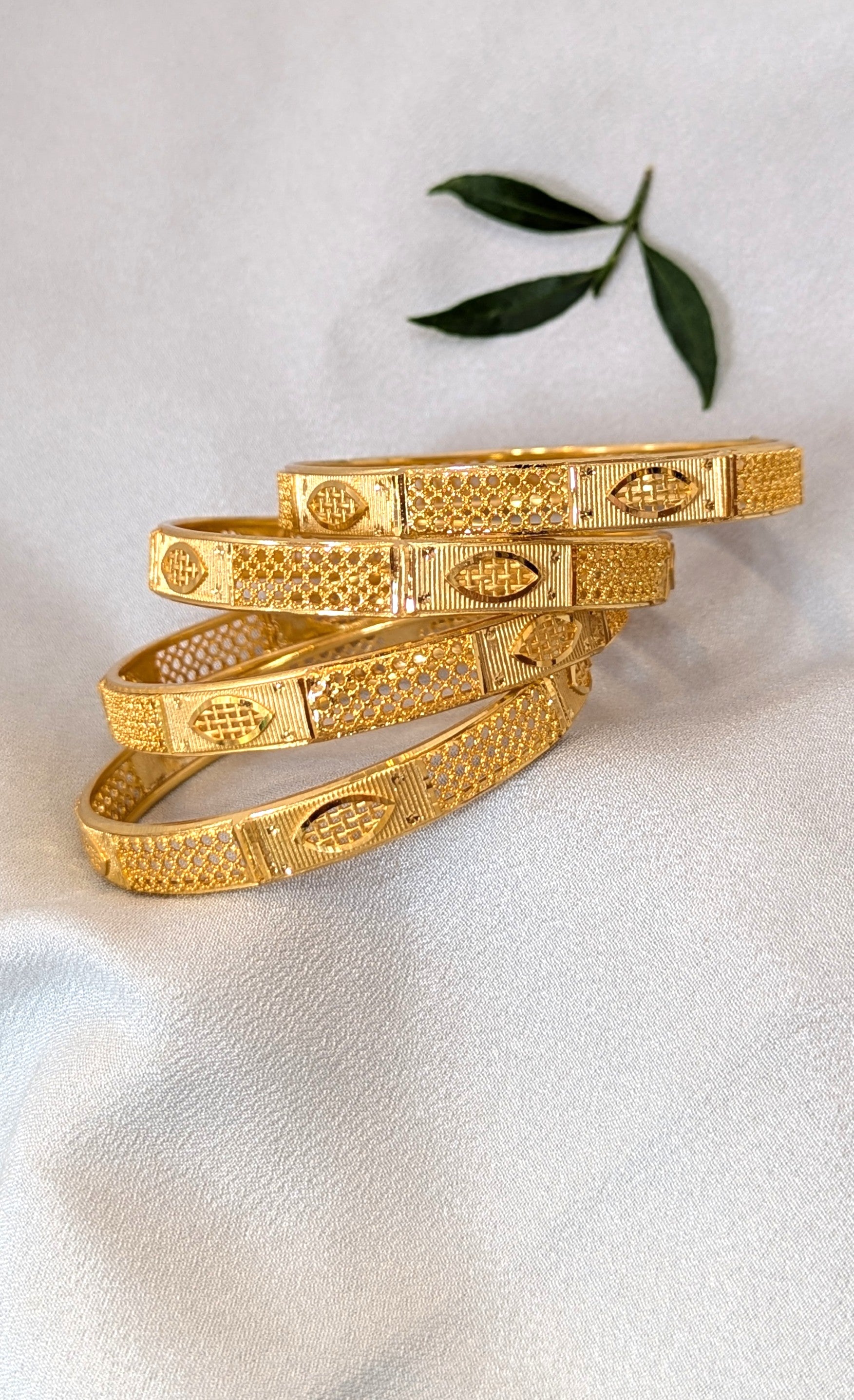 Stack of gold bangles on a white surface with a green leaf