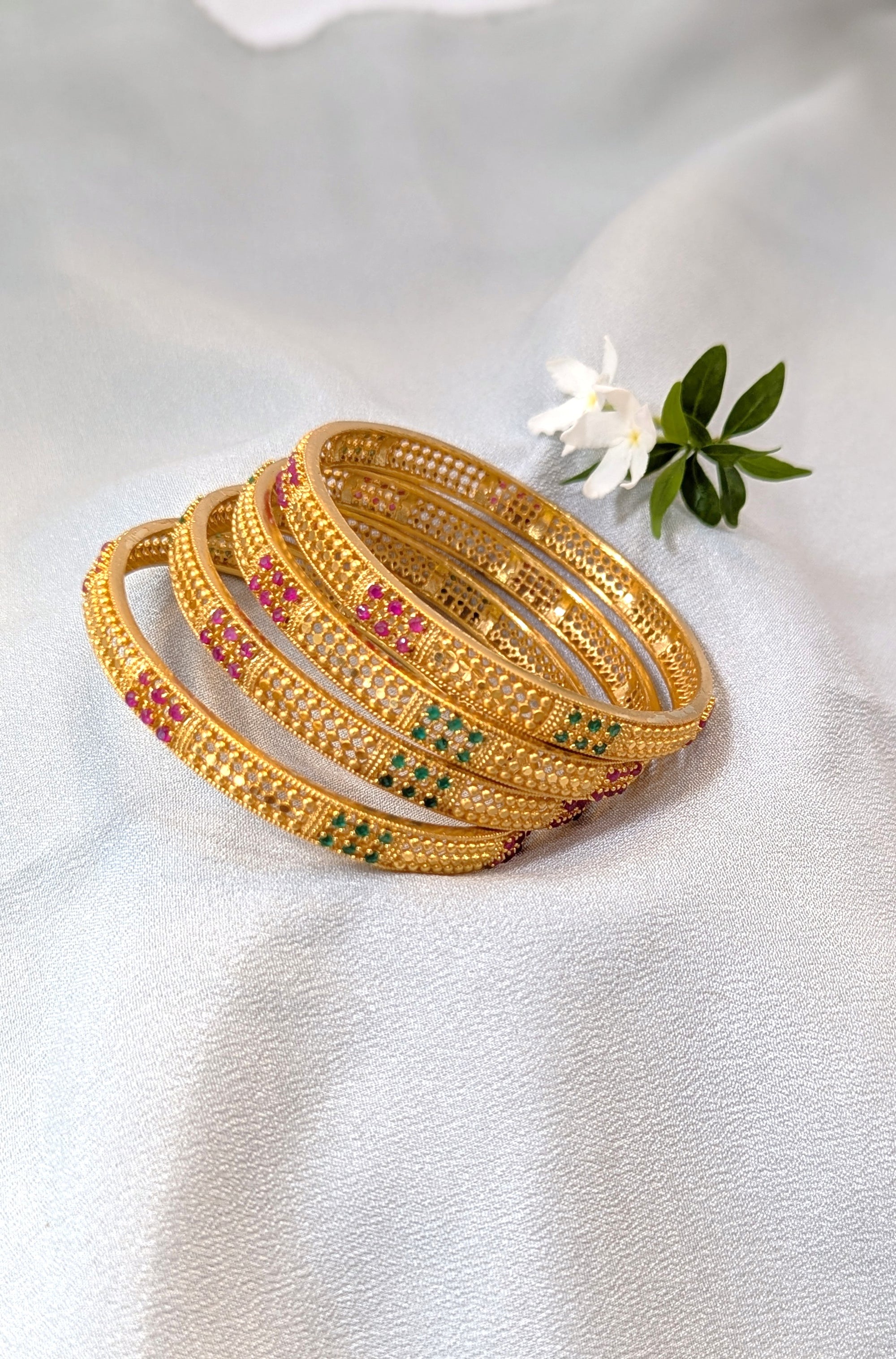 Set of gold bangles with gemstones on a white fabric background