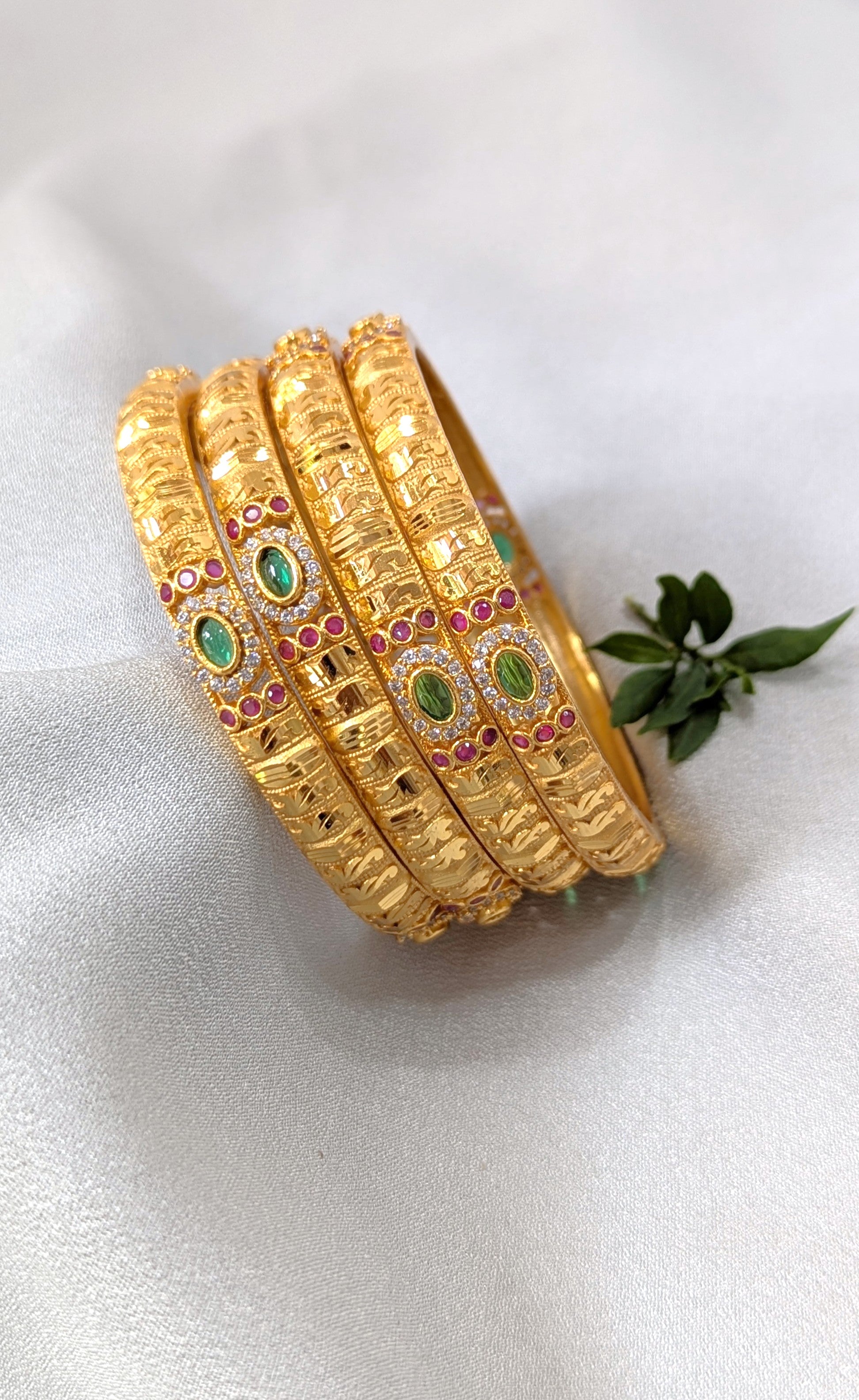 Set of gold bangles with green and red stones on a white background