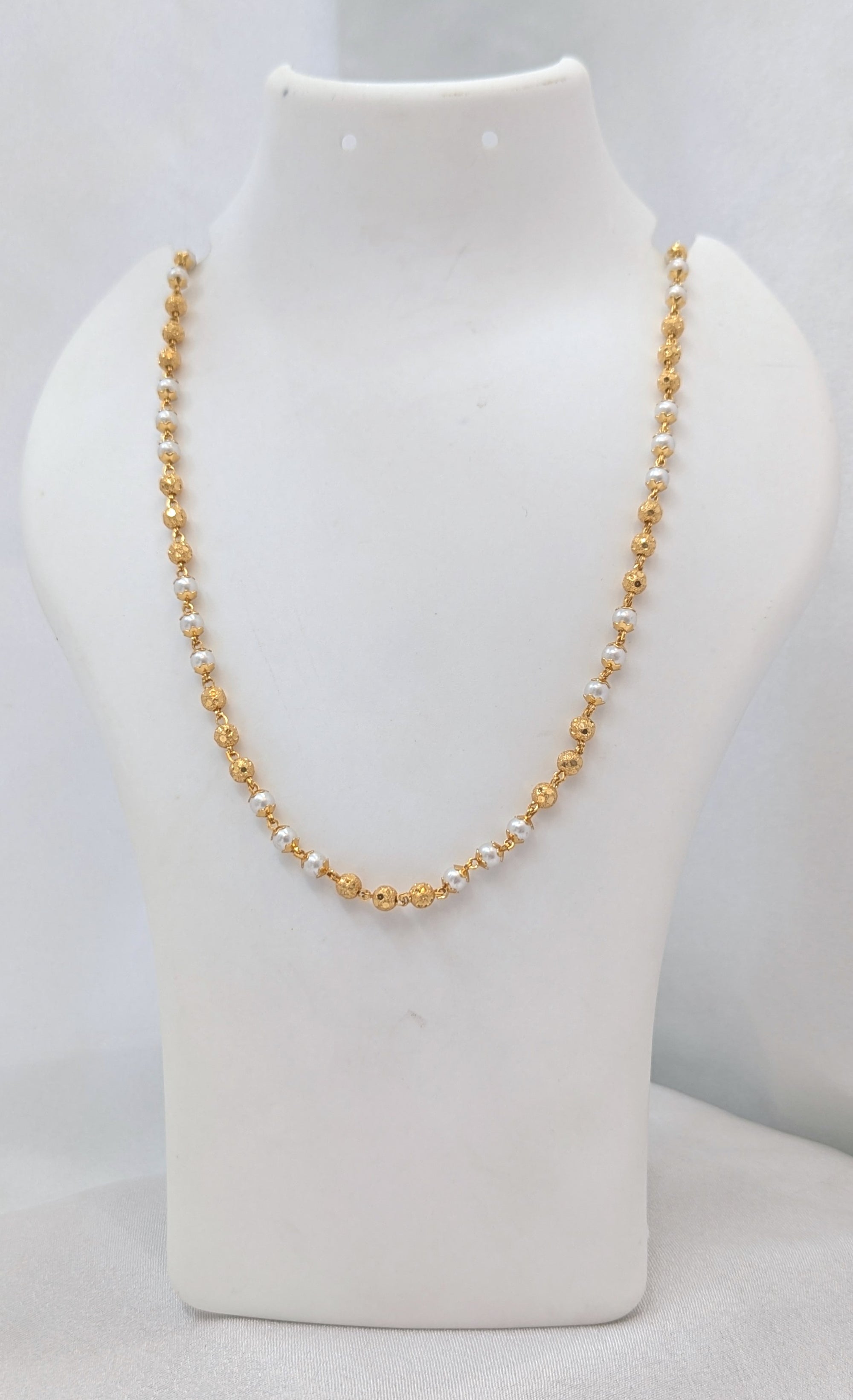 Gold and pearl necklace on a white mannequin bust against a white background