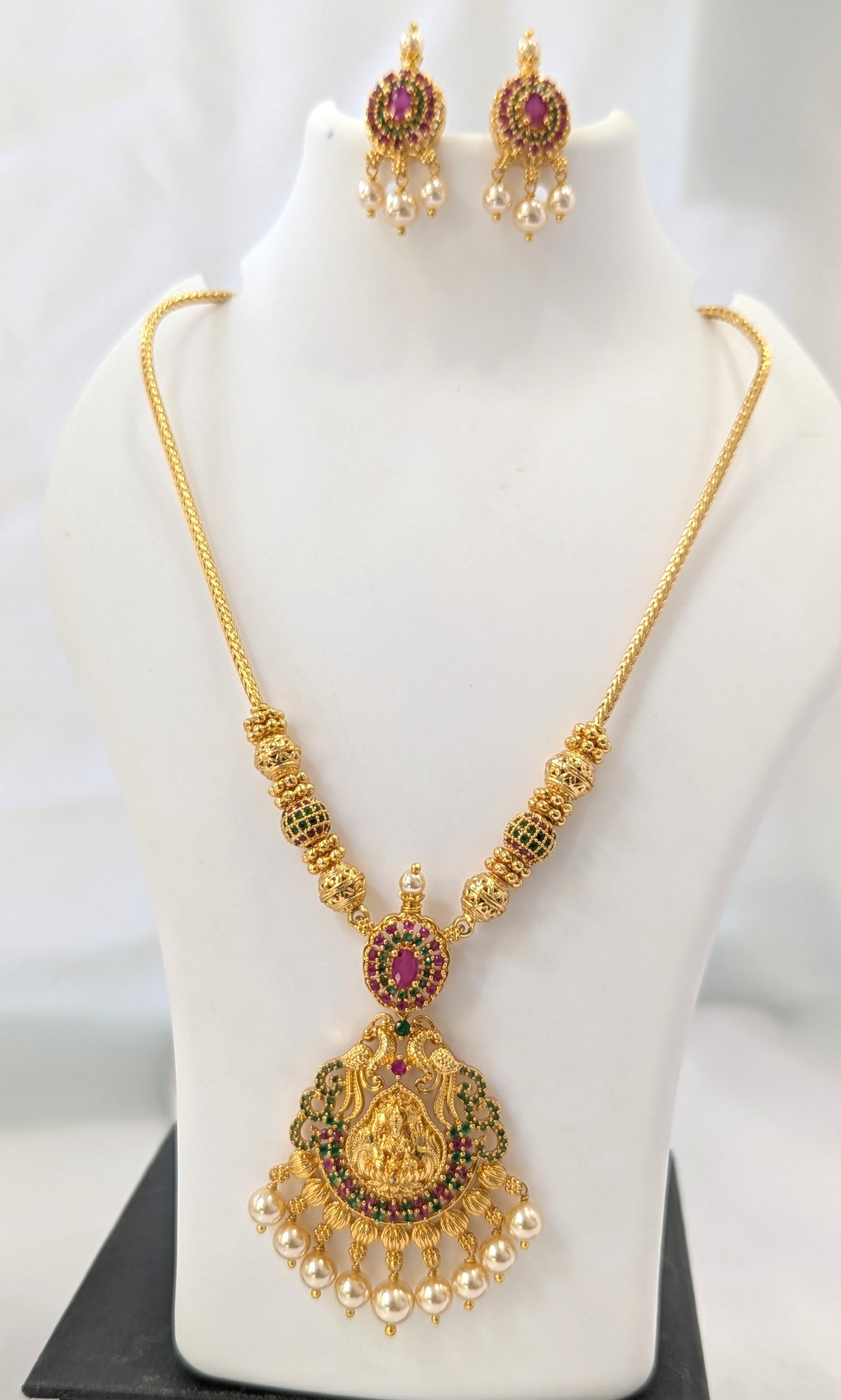 Gold necklace with pendant and matching earrings on a mannequin.