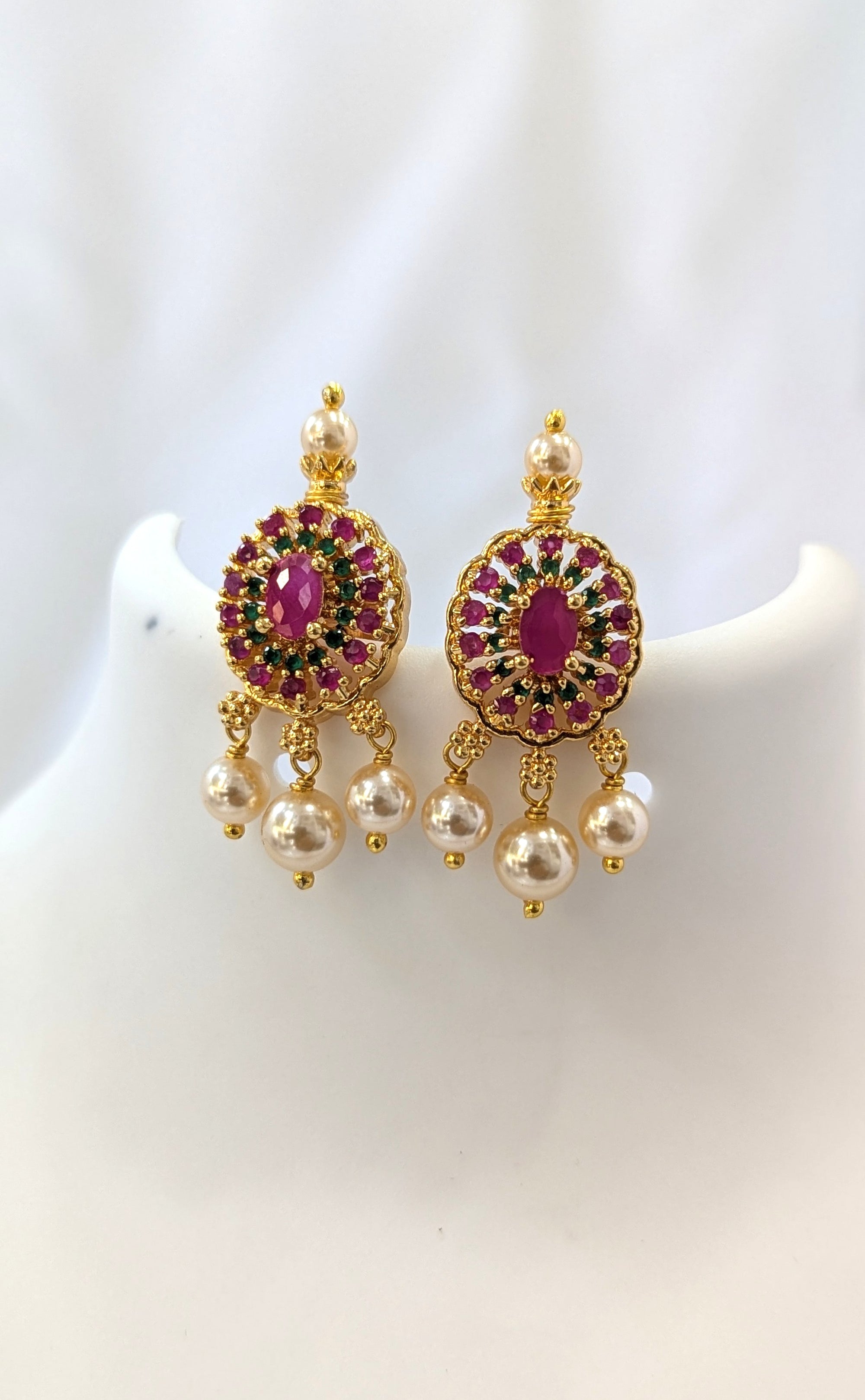 Gold earrings with red gemstones and pearl-like beads on a white background
