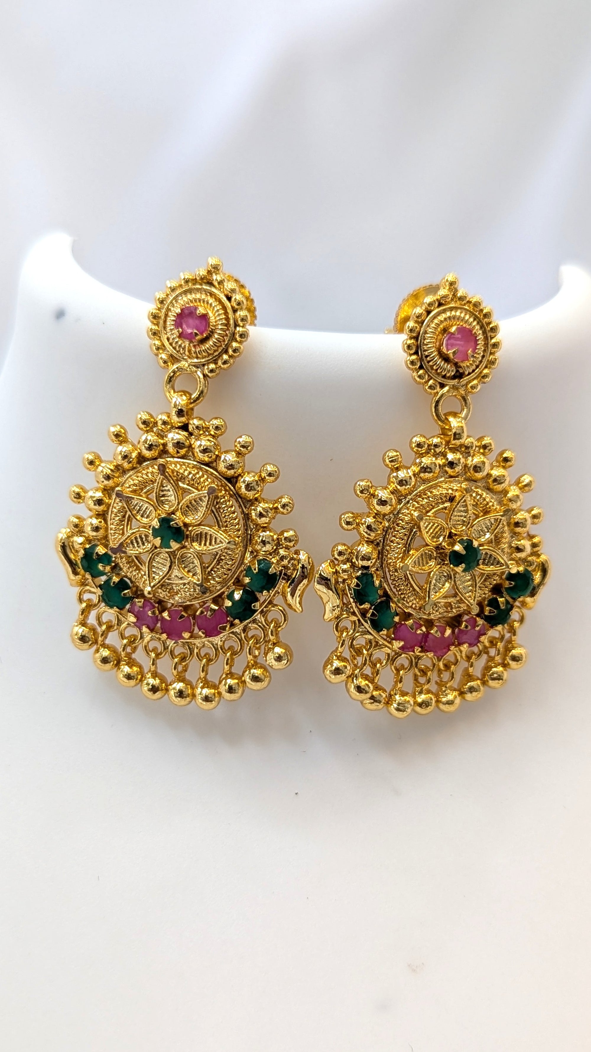 Gold earrings with pink and green stones on a white background