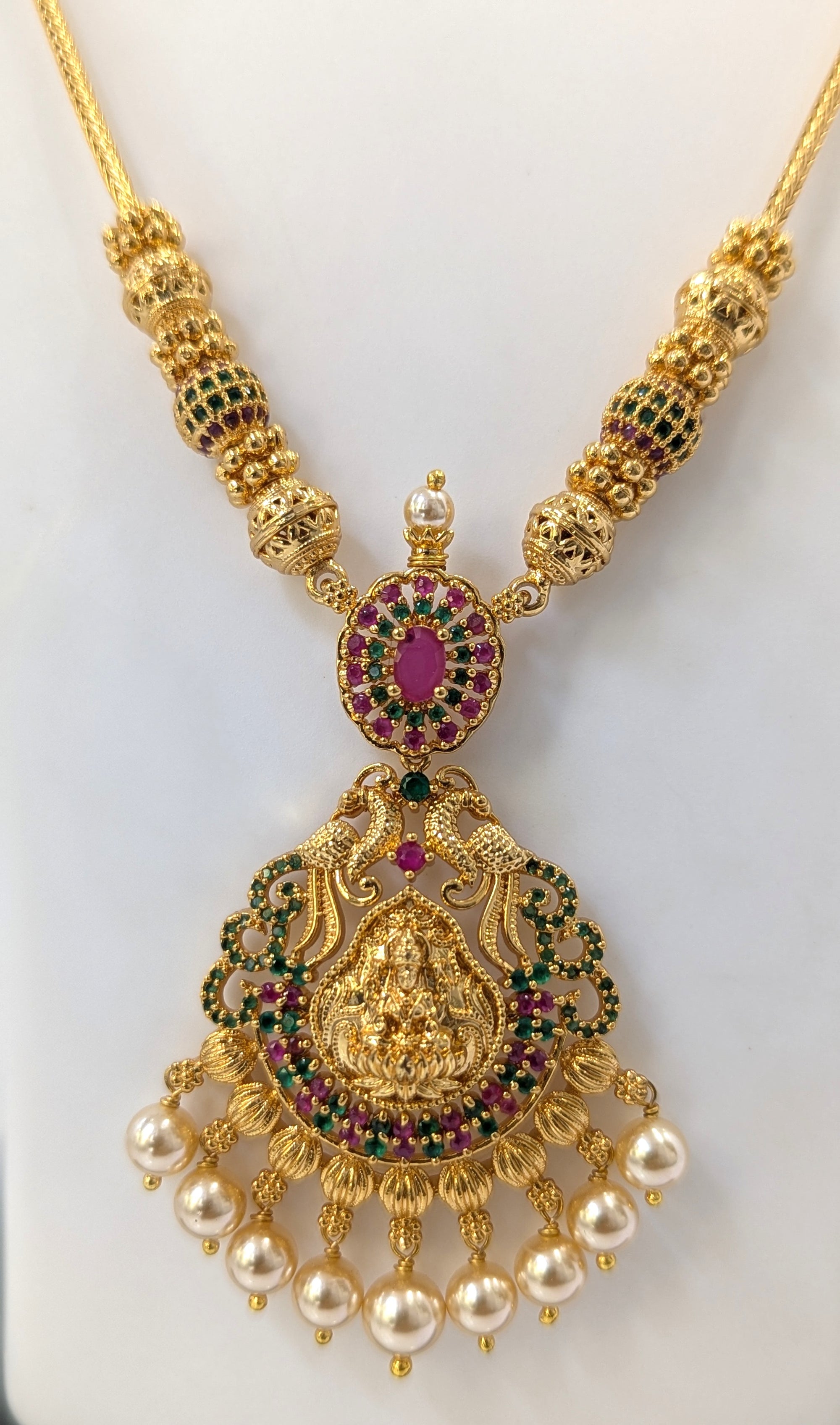 Gold necklace with intricate design and gemstones on a white background
